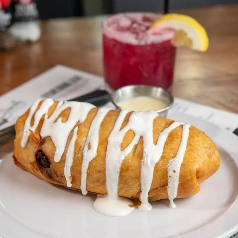 Breakfast chimichanga with sauce and a cocktail